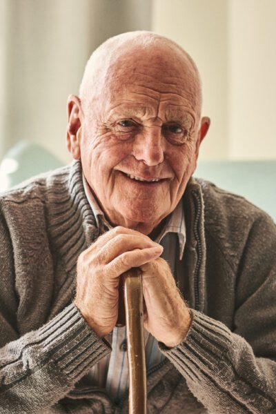 Portrait of happy senior man sitting at home with walking stock and smiling